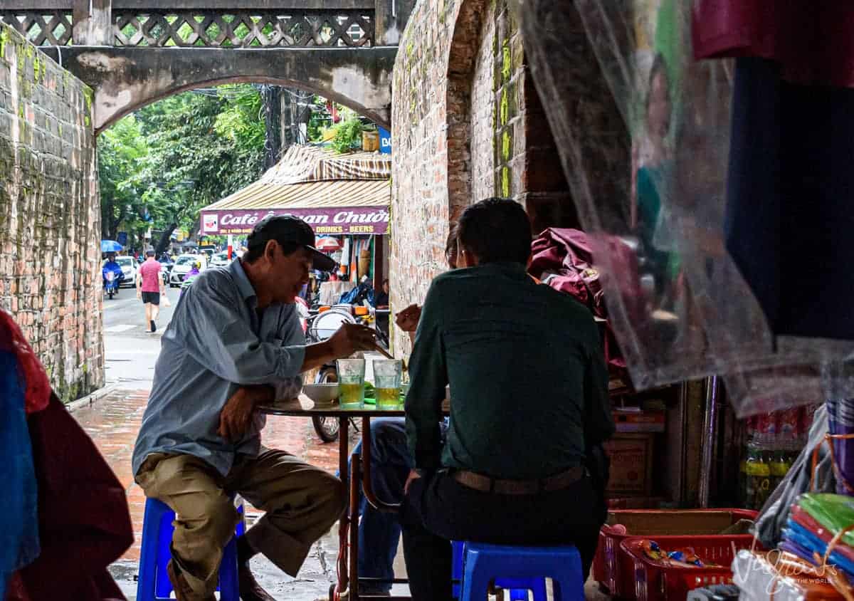 men on plastic stools enjoying lunch at an outdoor food stall.