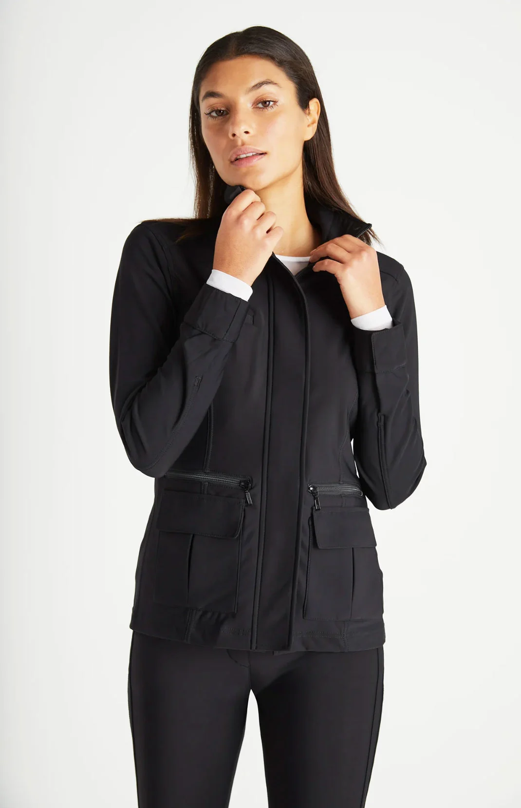 Attractive dark haired woman modelling a black travel jacket standing against a white wall. 