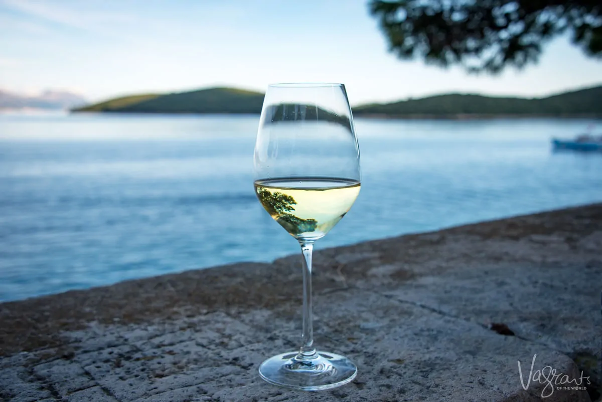 A glass of white wine on a ledge next to the ocean.