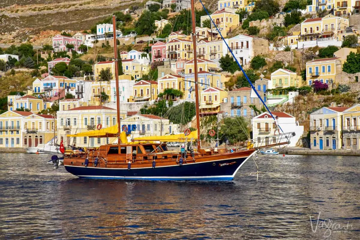 a motor yacht sailing past a hillside of old greek homes on Symi island. 