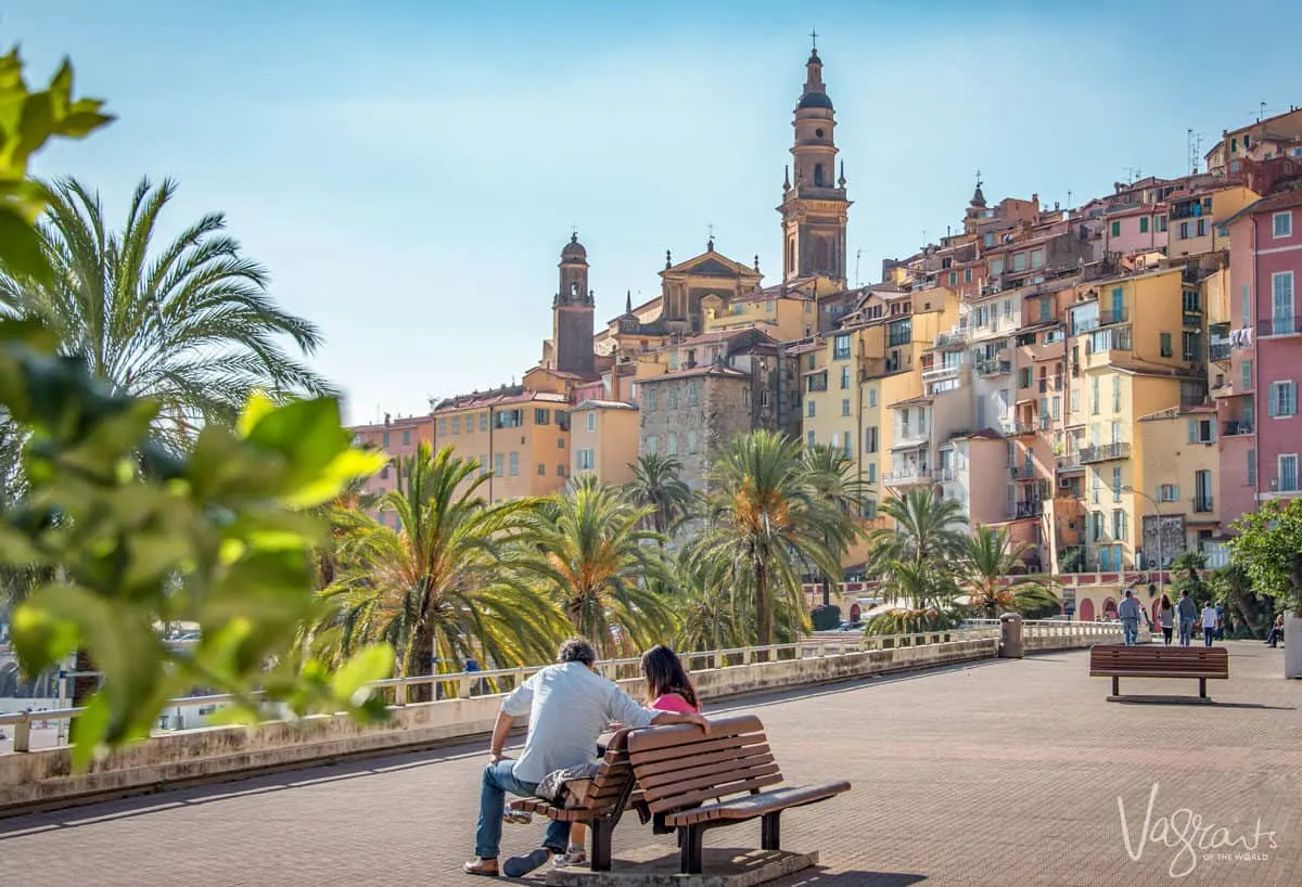 Couple sitting on a park bench with an old town in the background. 