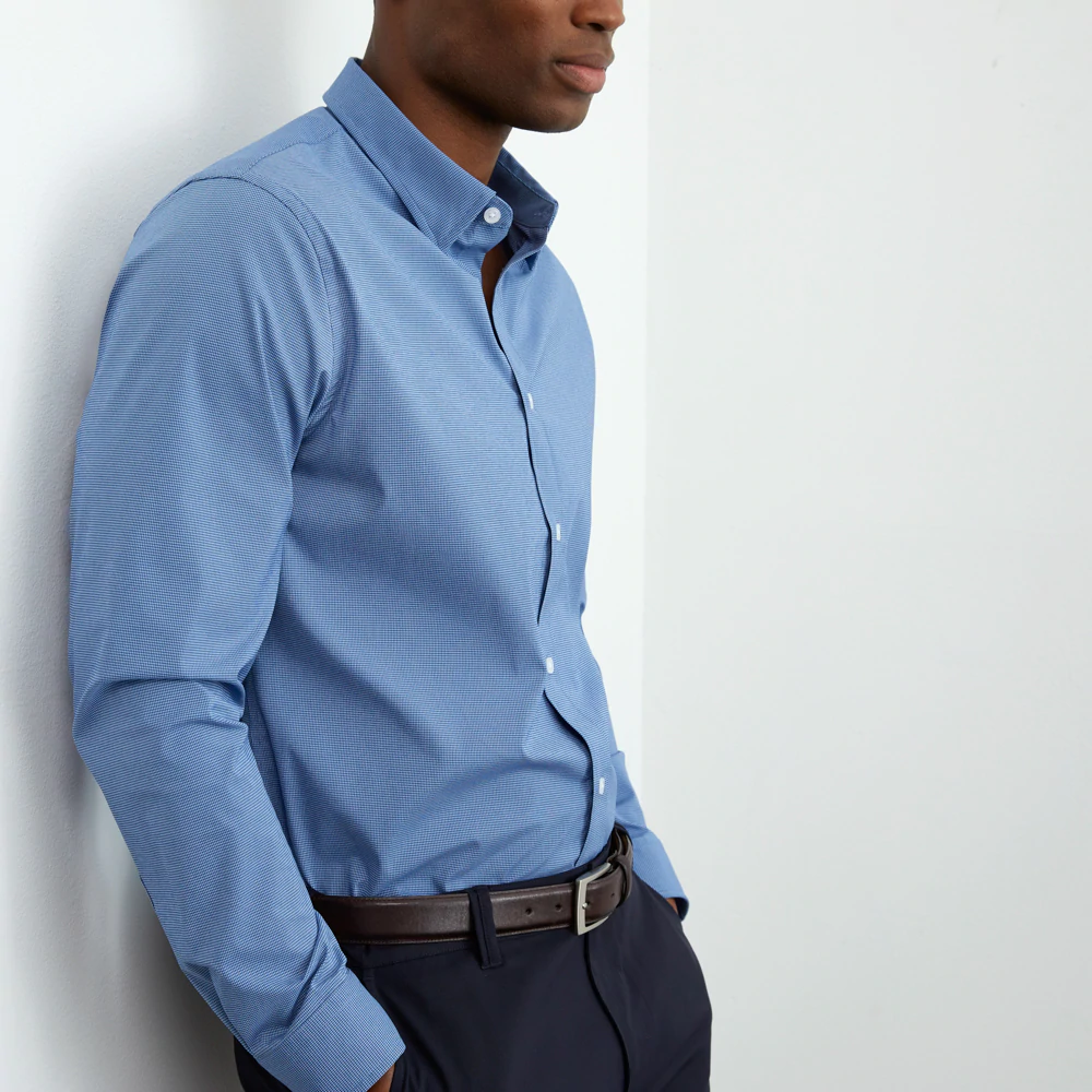 man in a blue dress shirt leaning against a wall.