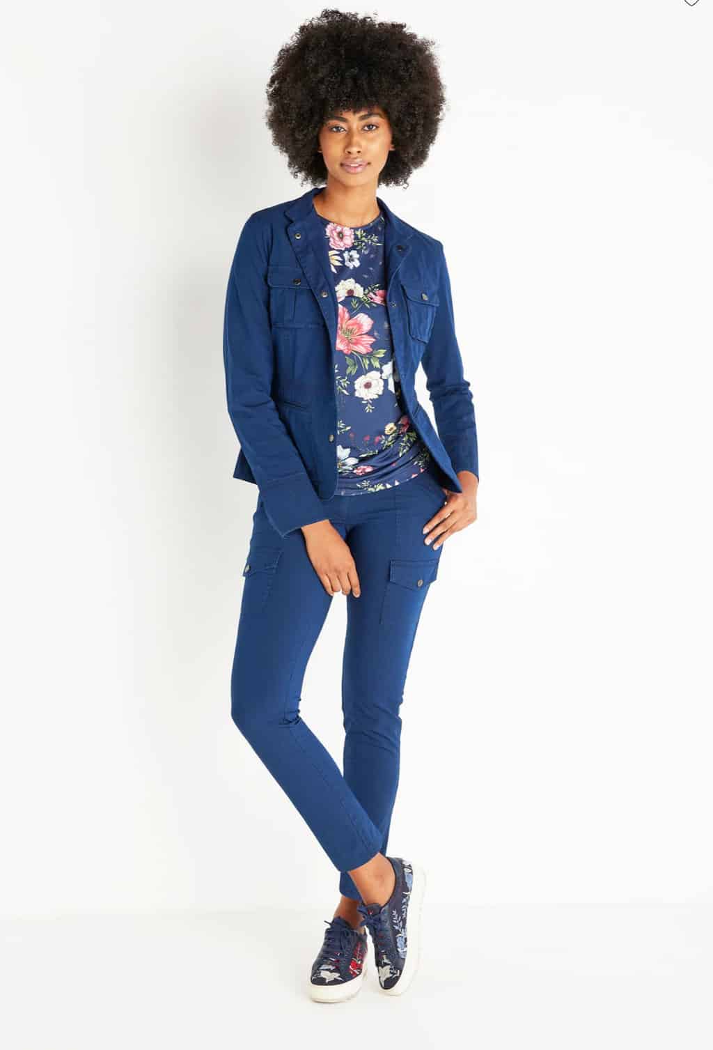 Attractive dark lady with a large afro modelling a blue denim travel outfit with a floral T-shirt and floral sneakers.