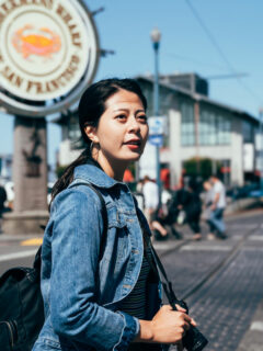 Asian female traveller crossing the street in San Francisco wearing a denim travel jacket.