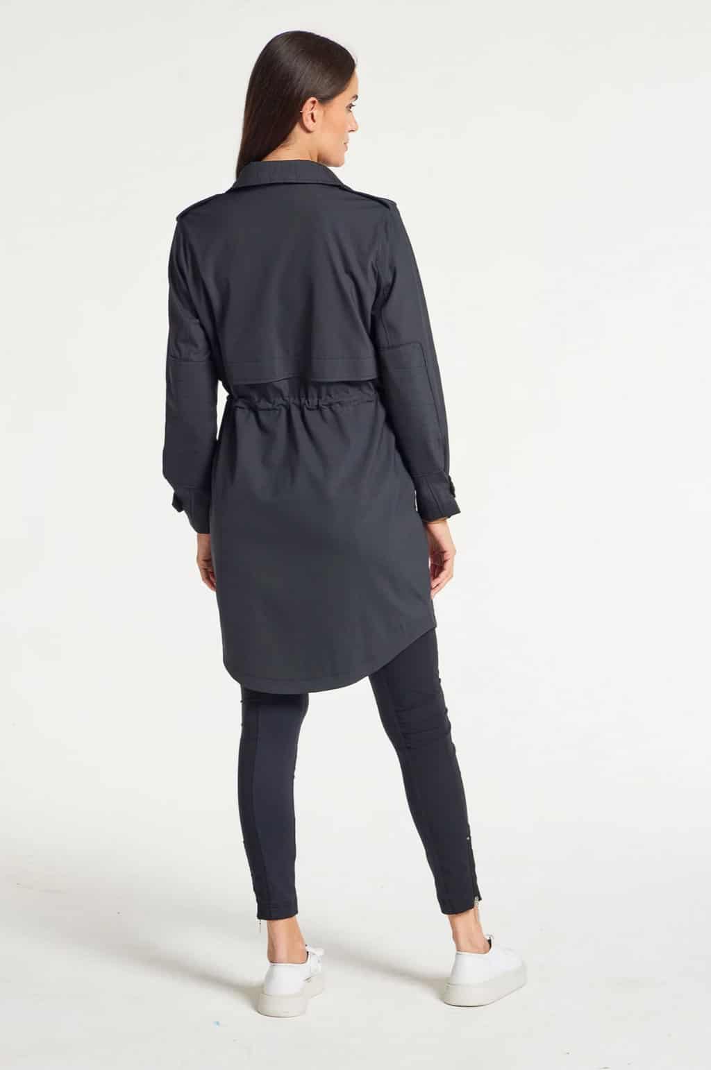 Back of a woman with dark hair modelling a travel trench coat.
