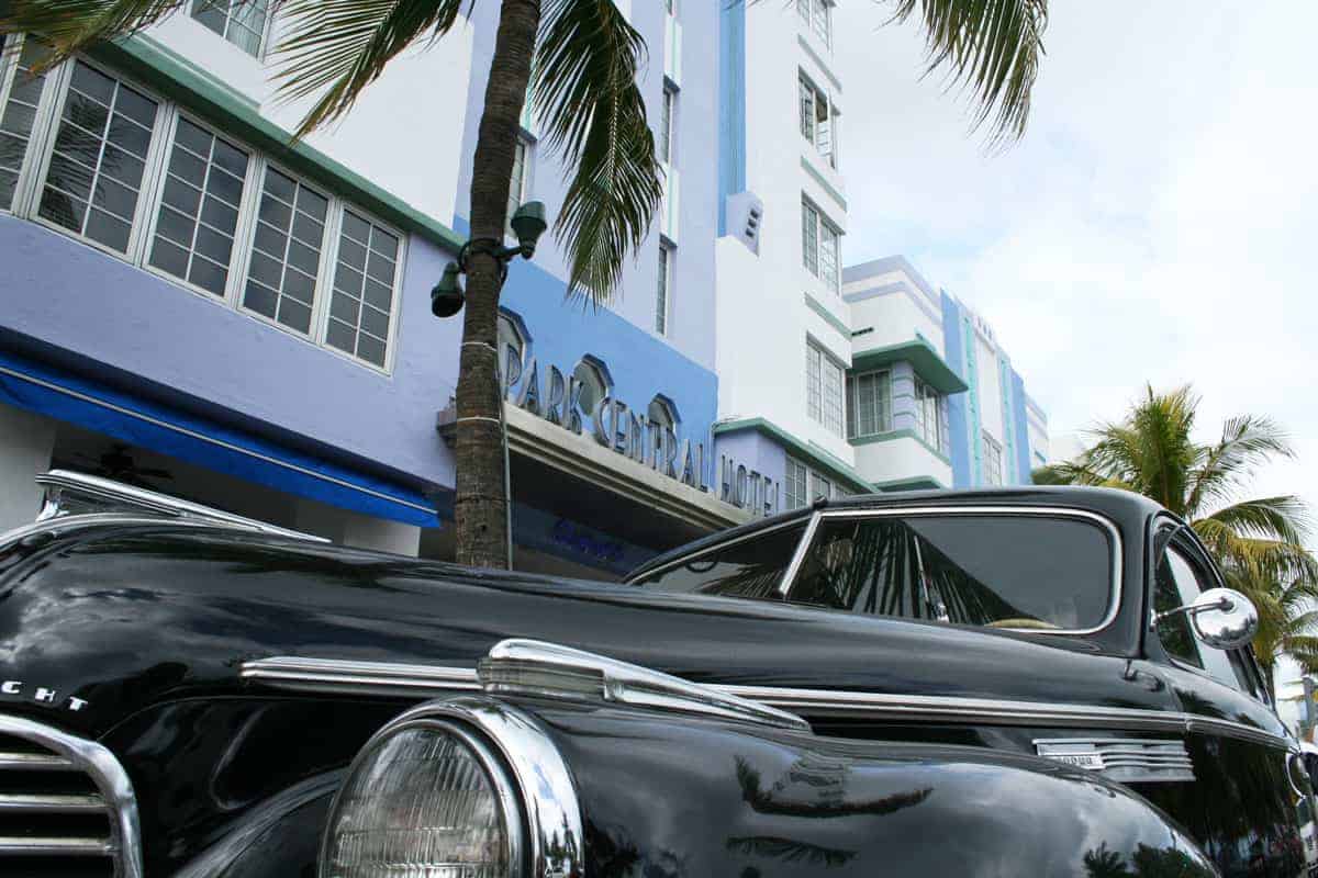 The bonnet of a black classic car with palm trees and one of Miami's iconic art deco hotels in the background. 