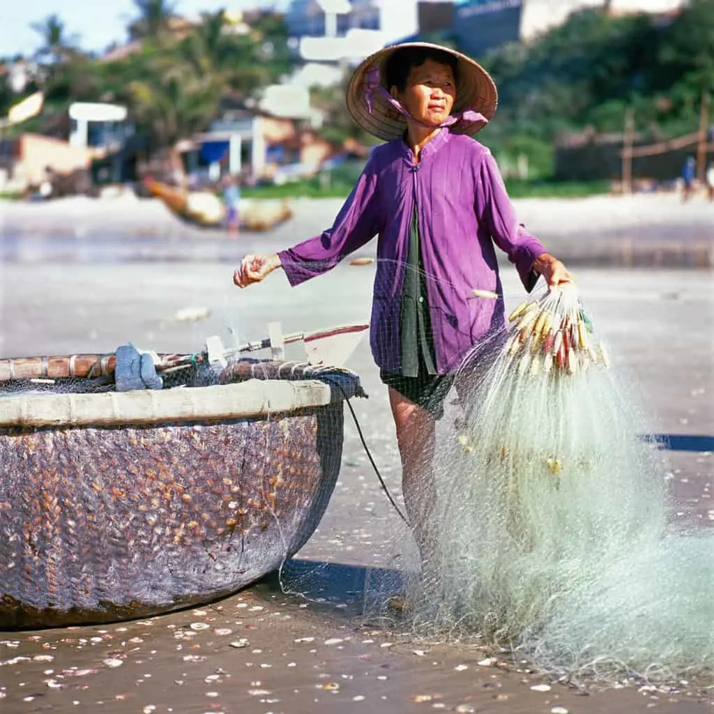 Local fisherwoman standing by a basket fishing boat holding a fishing net on the beach in Mui Ne Vietnam