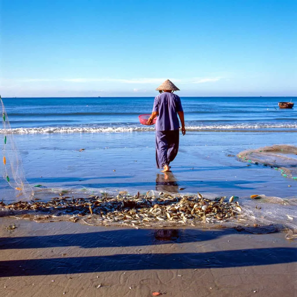 Fisherman standing on the beach with fishing net loaded with fish on the sand .