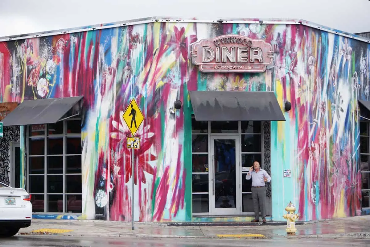 Man standing out the front of a typical american diner brightly painted with murals. The street art of Wynwood Diner. 