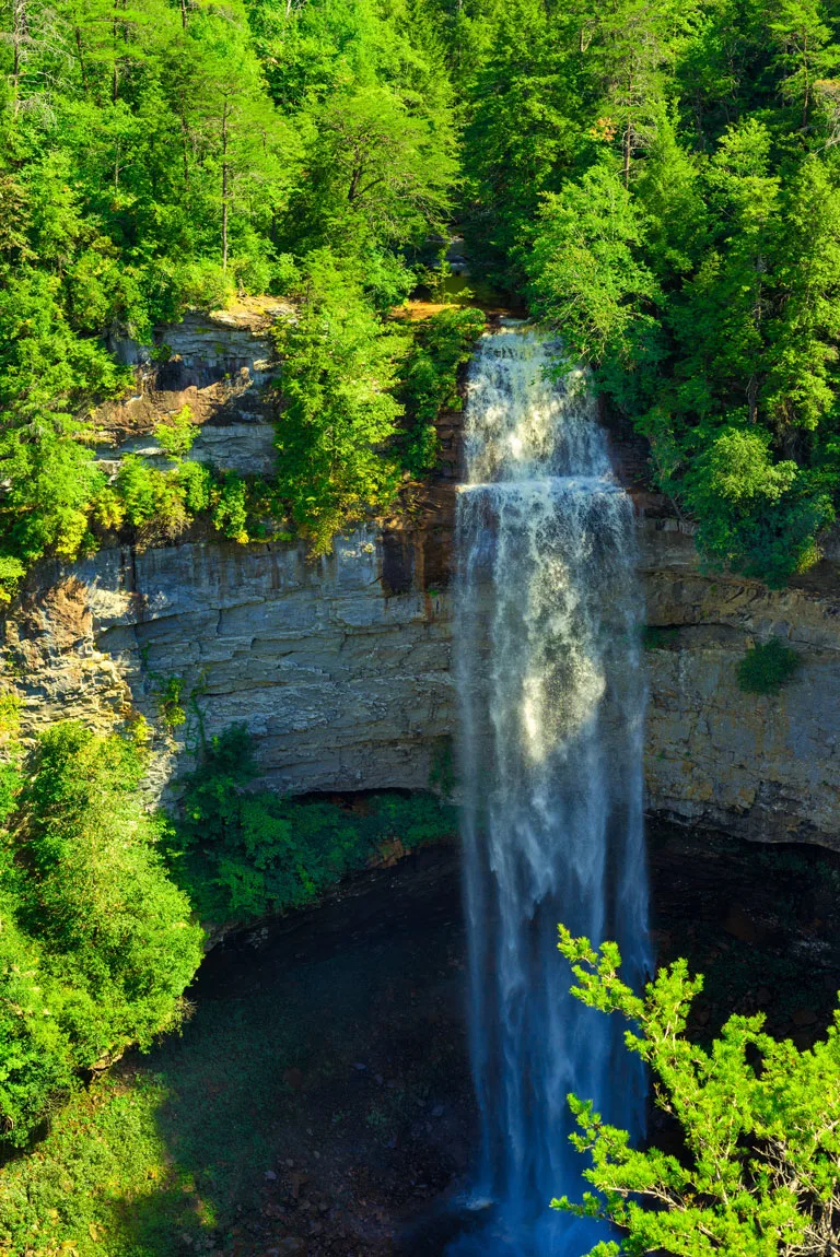 Looking over the water drop of Fall Creek Falls in Tennesee surrounded by green trees. 