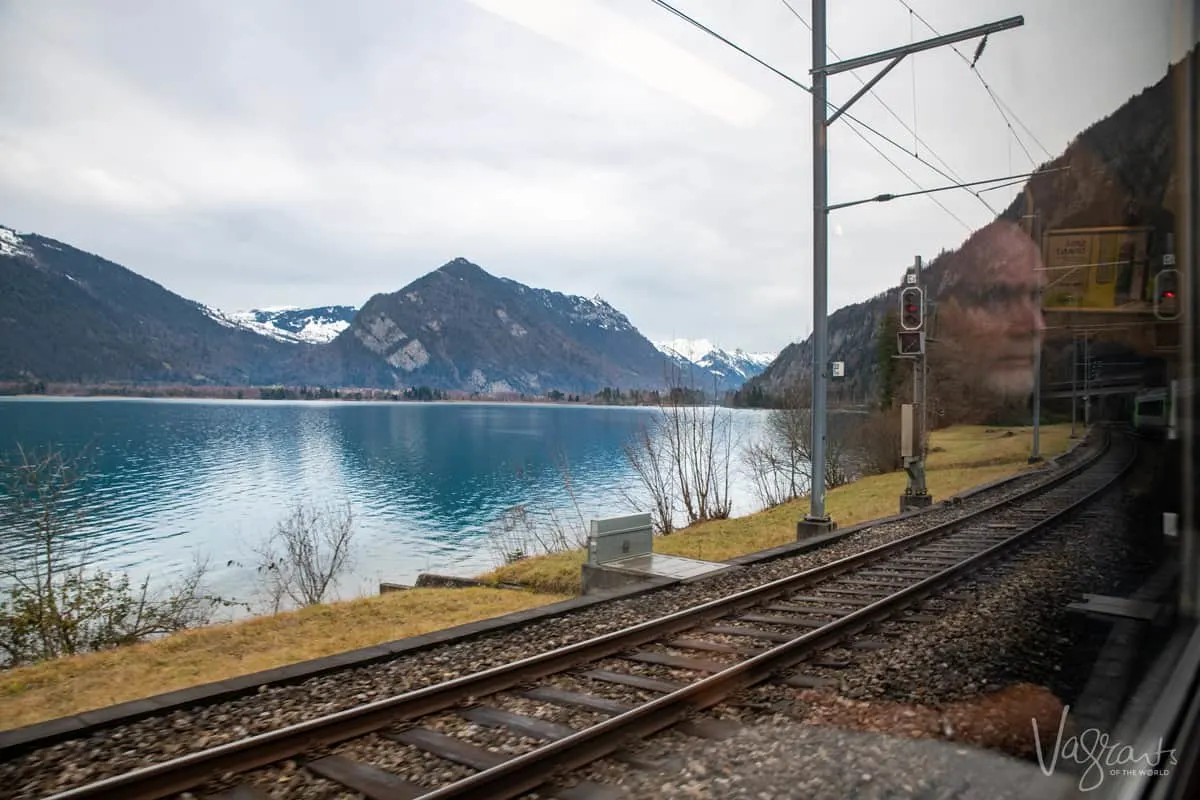 Reflection of man in a train window looking over a clear blue lake and alpine landscape on the Golden Pass Train in Switzerland, one of the most scenic train routes in the world. 