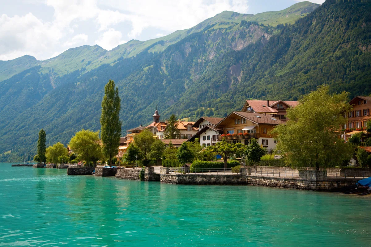  turquoise lake and a typical swiss village on the water surrounded by green hills, these are some of the most best places to visit in Switzerland
