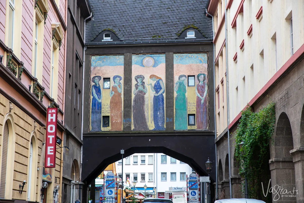 Looking at an arch way in the old town with painted panels above the arch depicting women in the old town of Koblenz Germany. 