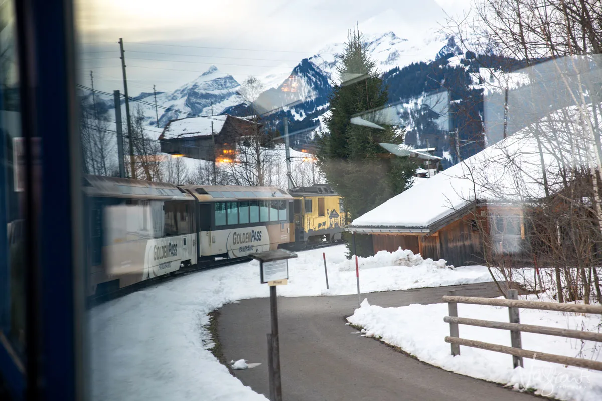 Train window view on a bend towards the front of the panoramic train on the Golden Pass line as it passes through a snowy alpine village in the Swiss Alps