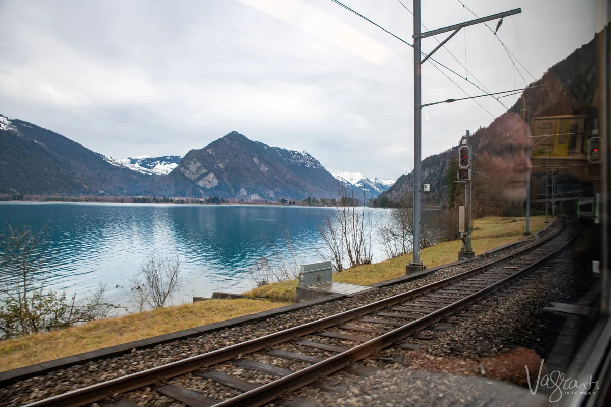 Reflection of a man in the window of a train looking out over a crystal blue lake in Switzerland travelling on the Golden Pass Railway