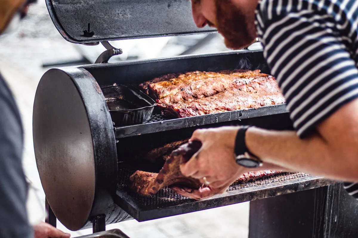 man pulling smoked ribs out of the smoker at the Crescent Music and BBQ Festival