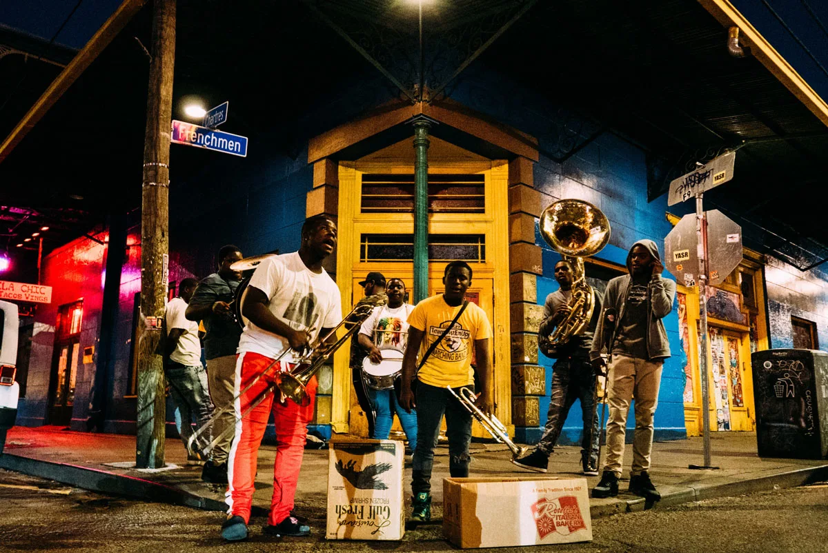 A group of buskers standing in front of brightly coloured houses on Frenchman street New Orleans