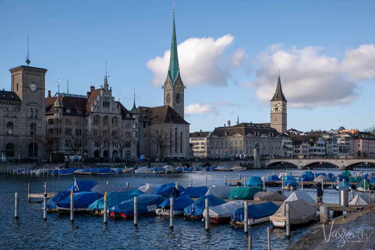 Boats moored in the foreground in front of Zurich City with clock tower spires on the skyline. 