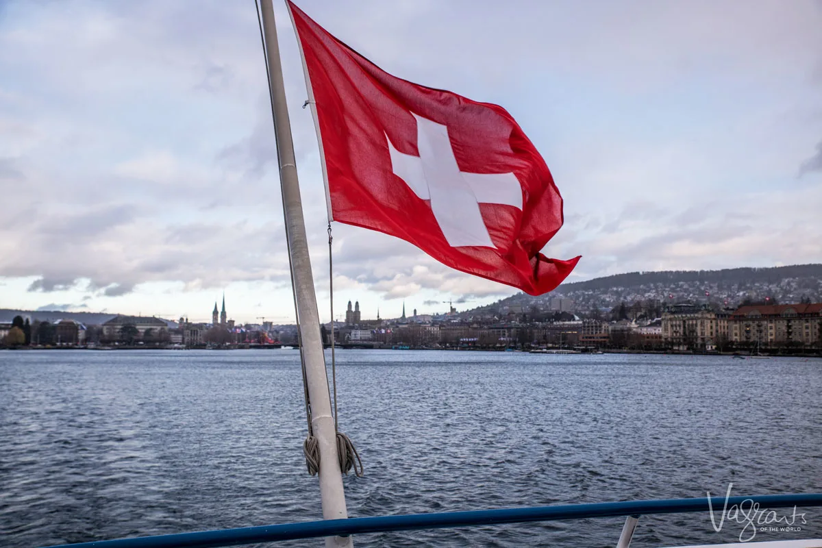 View of the Swiss flag from the back of a ferr looking back at Zurich city