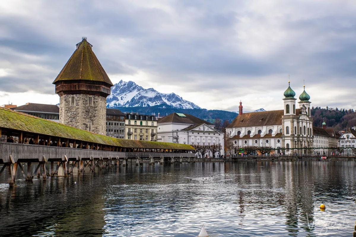 Lucerne Old Town with the covered wooden bridge and tower in the foreground and the Swiss Alps on the skyline.