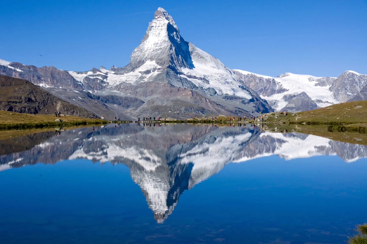 Matterhorn perfectly reflected in the lake with tourists standing in front. 