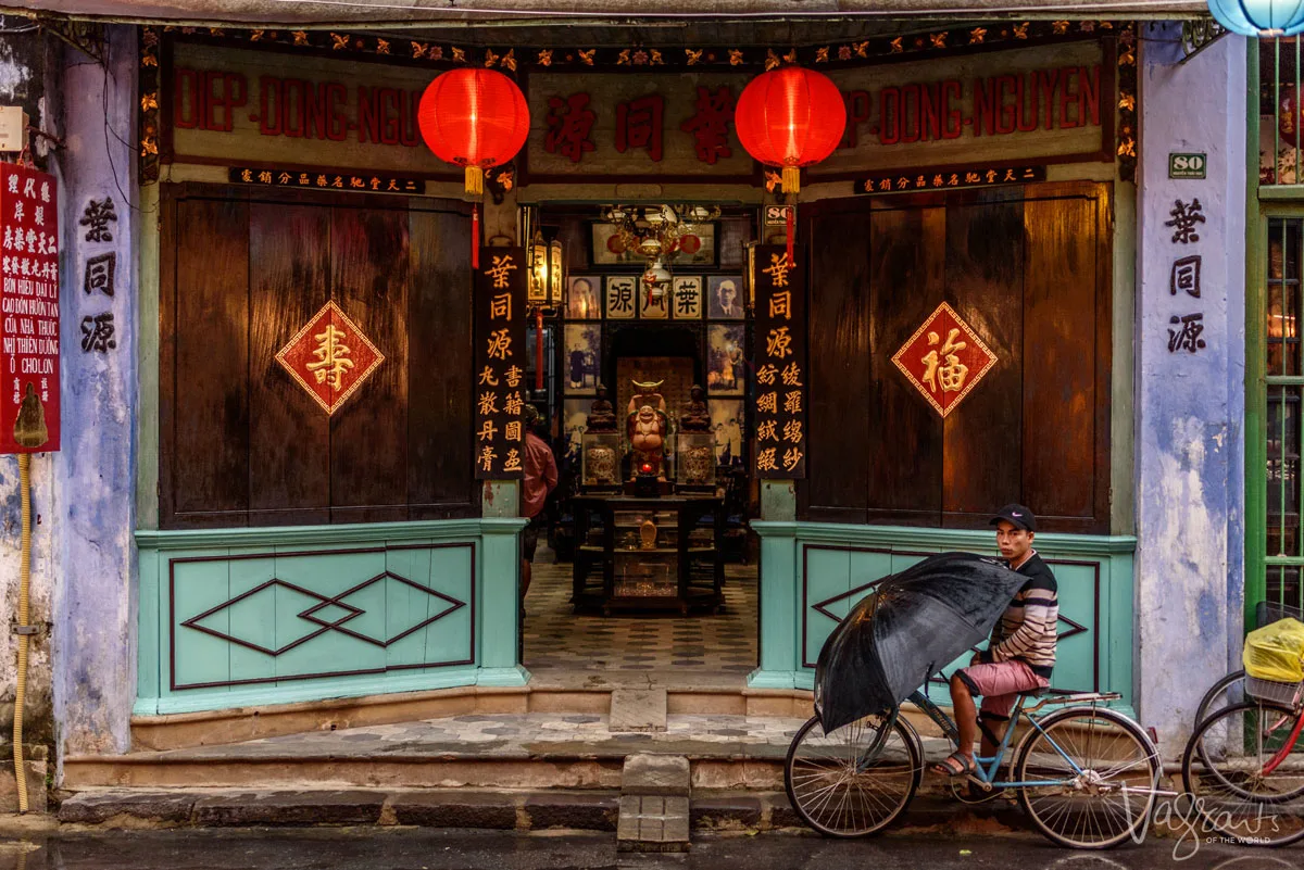 Vietnamese man on a bicycle holding an umbrella outside a heritage buddhist temple in Hoi An Old Town
