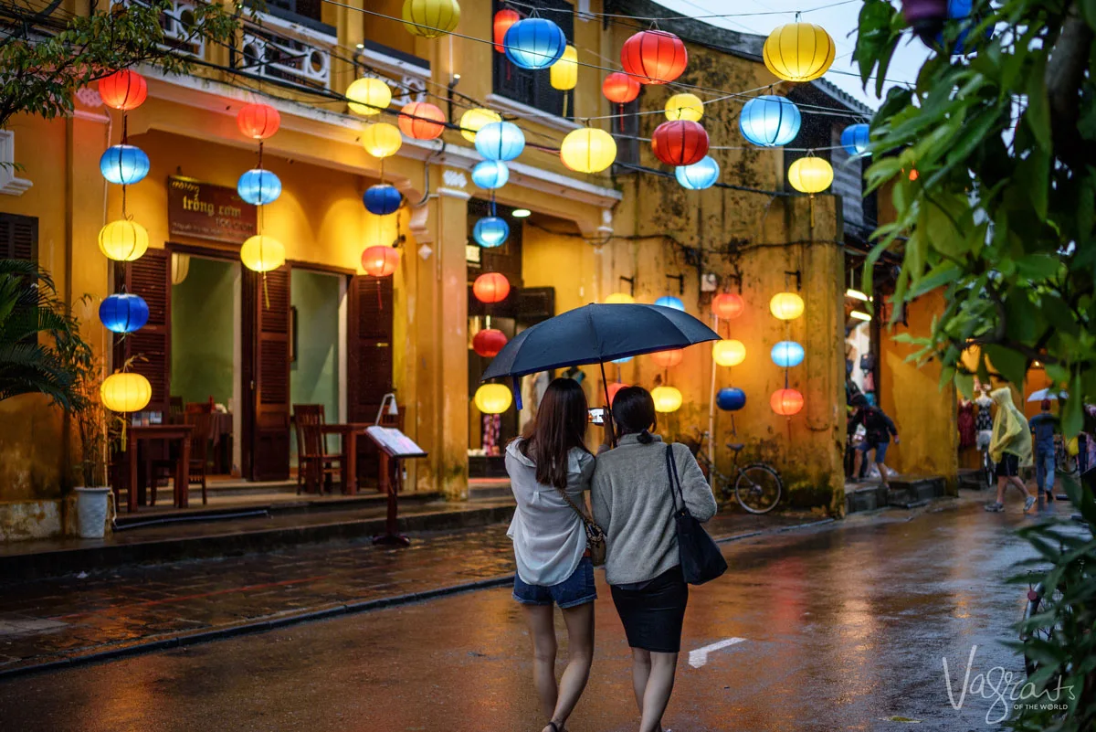 two girls under an umbrella strolling down the street shopping and looking at the lanterns at night in Old Town Hoi An. 