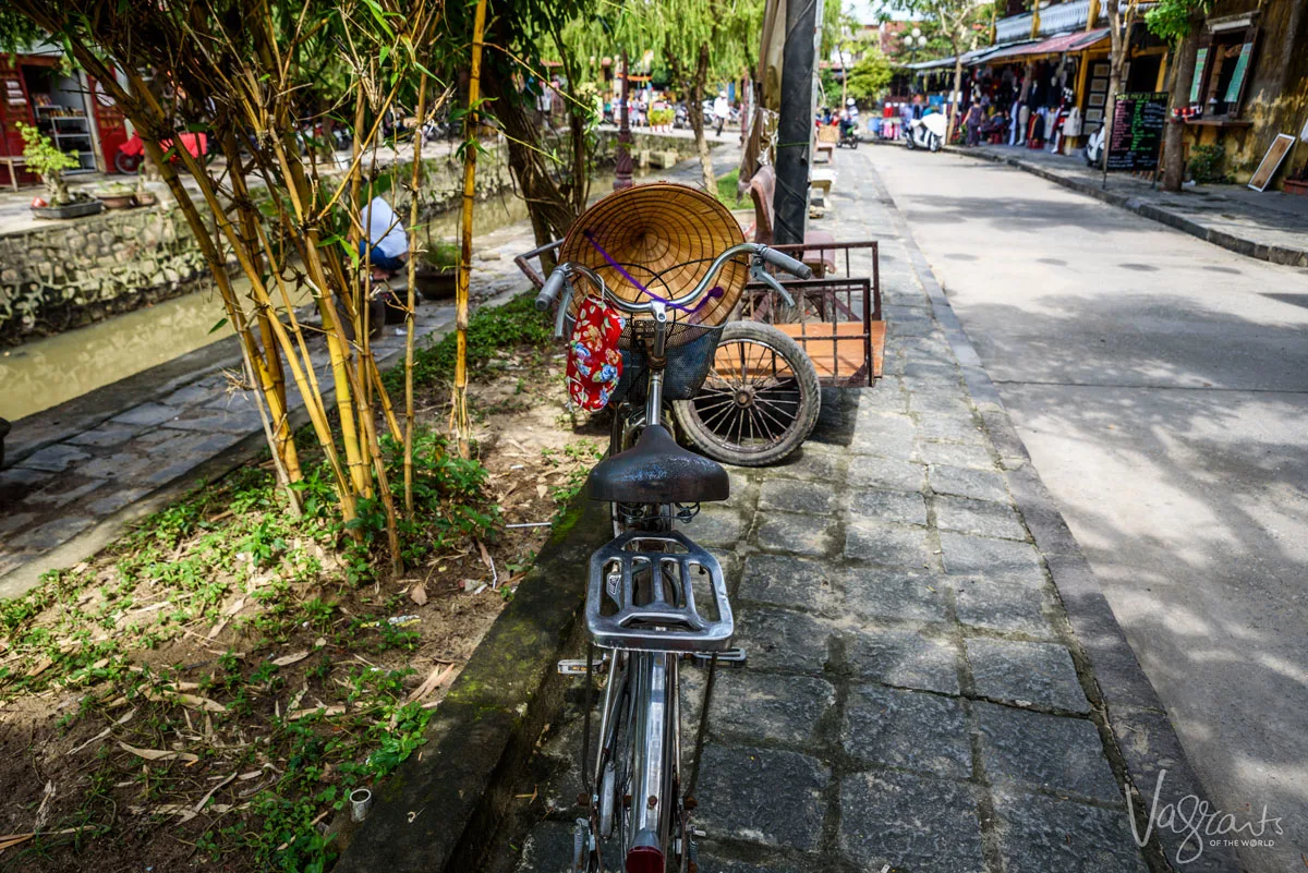 Bicycle on the side of the road in Hoi An with a traditional Vietnamese conical hat hanging from the handle bars