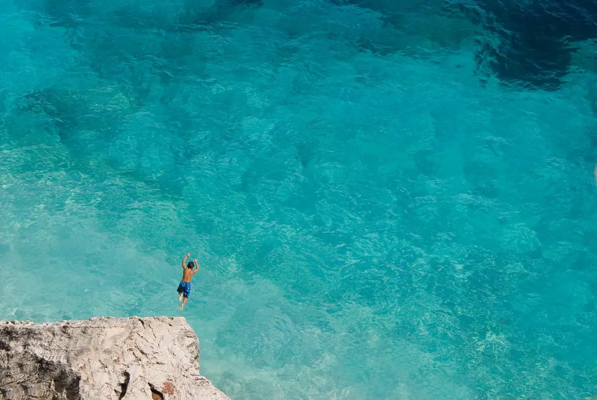 Man diving off a rock into crystal clear sea water in Sardinia