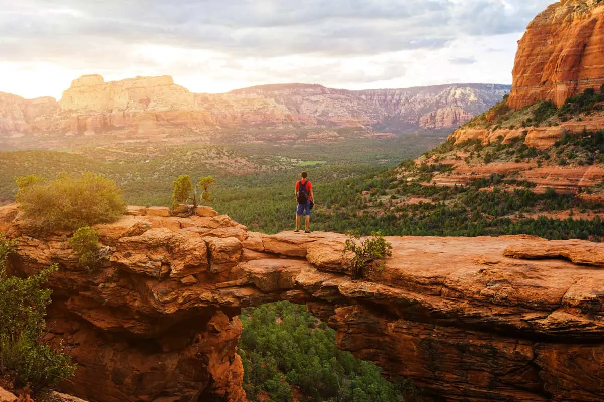 Hiking man on the natural rock bridge - Devil's Bridge in Sedona at sunset. 