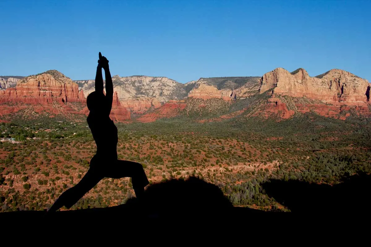 Silhouette of a person in a yoga pose on a red rocky outcrop 