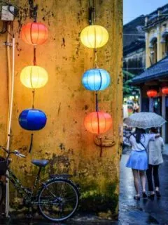 Two girls under an umbrella walking down the lantern filled streets of Hoi An Old Town at night. 2 Days in Hoi An never feels like enough.