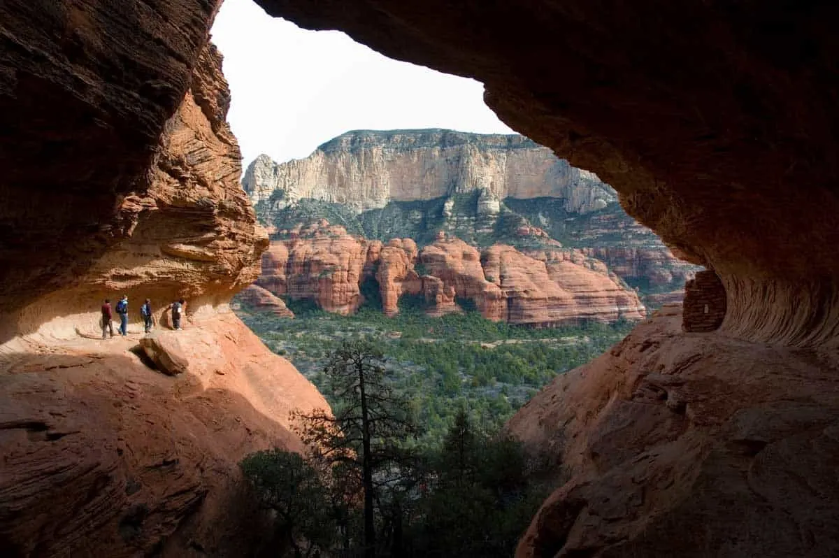 Looking through a natural rock window at a group of people hiking the red rock trails in Sedona in Arizona. 