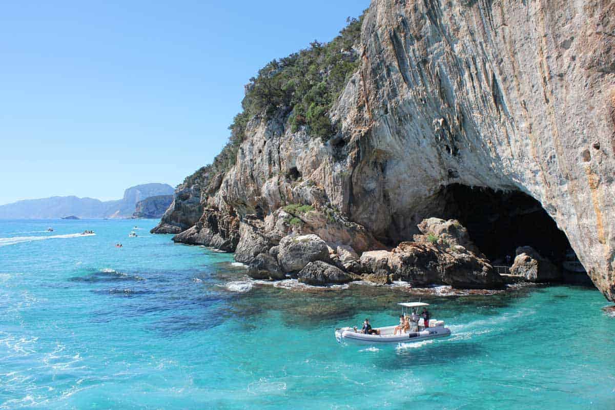 A Sardinia sailing and boating tour floats outside a cave on crystal clear waters. 