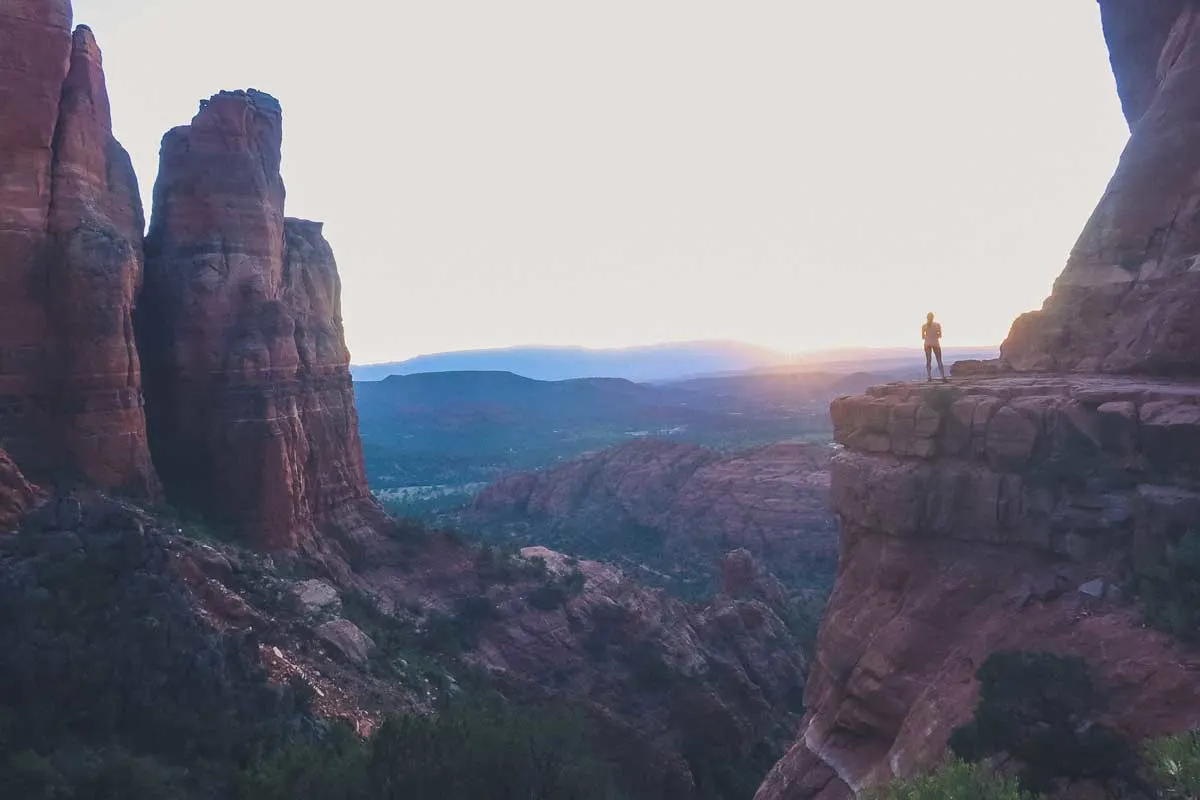 Girl standing on rocky outcrop over a large canyon at sunset. 