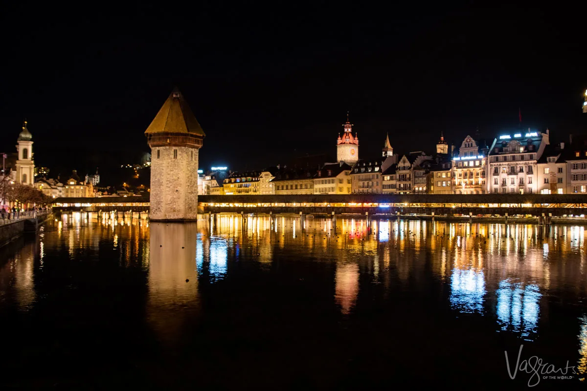 Covered wooden bridge at night with Lucerne Old Town lit up in the background