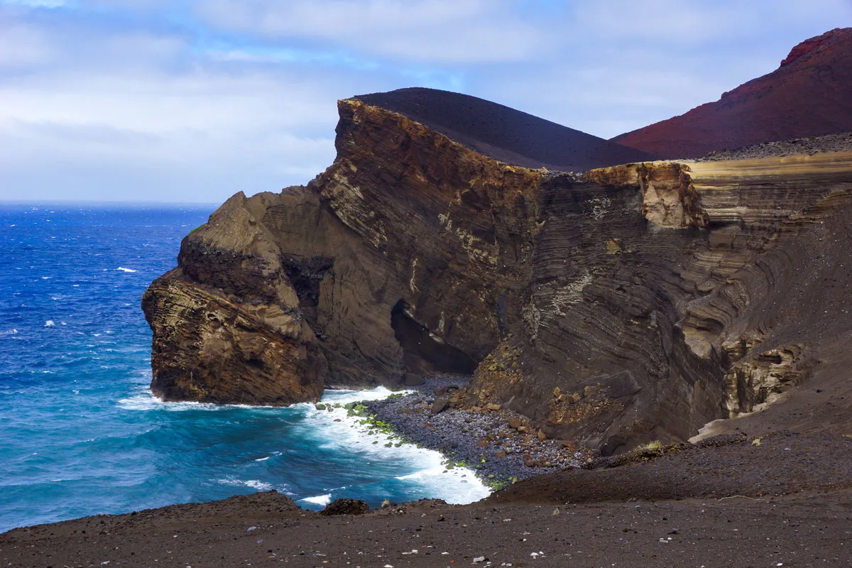 Lava beach and cliff against dark blue sea.