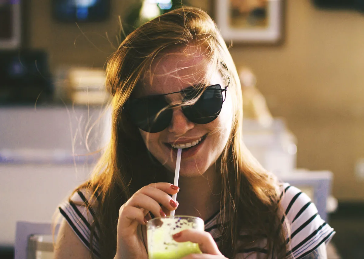 A portable blender for travel can keep you healthy and save you money like this girl drinking a smoothie.