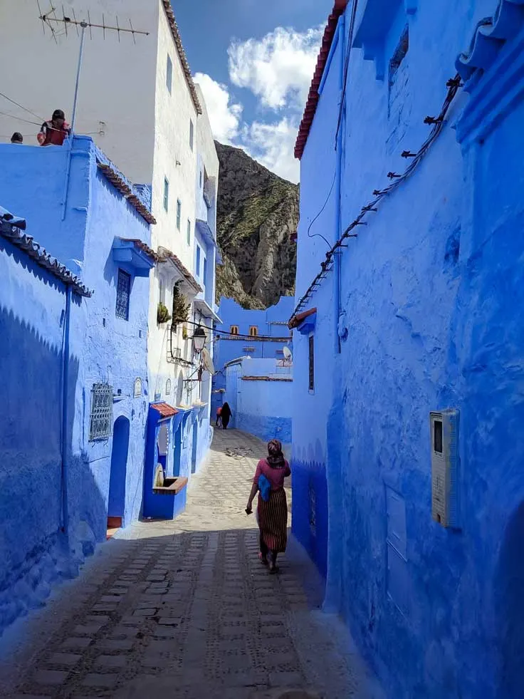 Tourist walking down blue walled alley in Chefchaouen.