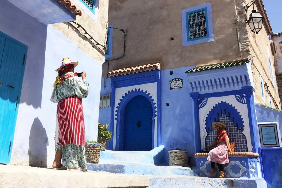 Moroccan girls in traditional dress outside blue house in Chefchaouen.