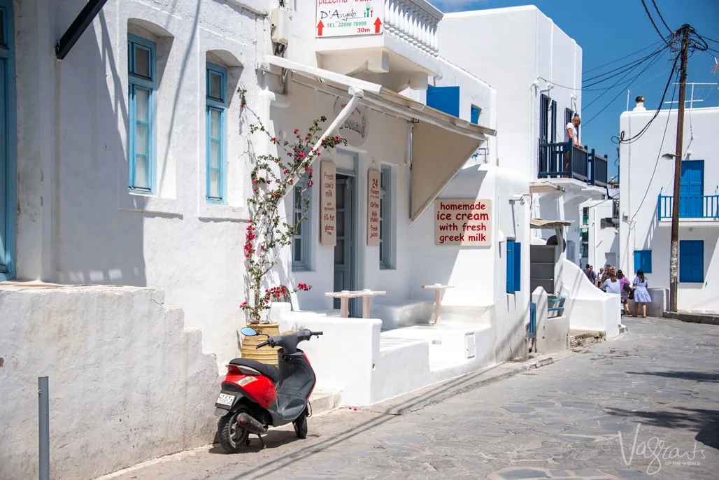 Scooter parked outside whitewashed shops selling ice cream made with greek milk.