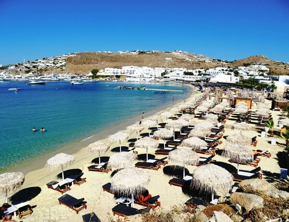 Ornos beach covered in beds and parasols inviting tourists to Mykonos for the summer.