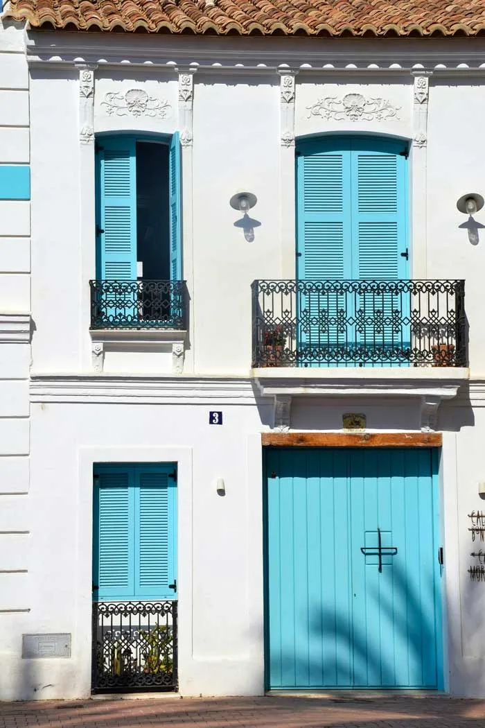 Sky blue shutters and doors behind iron railings of a white house in Valencia.