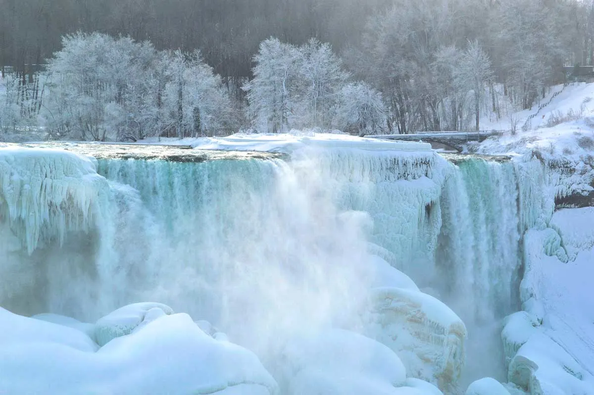 Blue ice over Niagara Falls and snow covered forest.