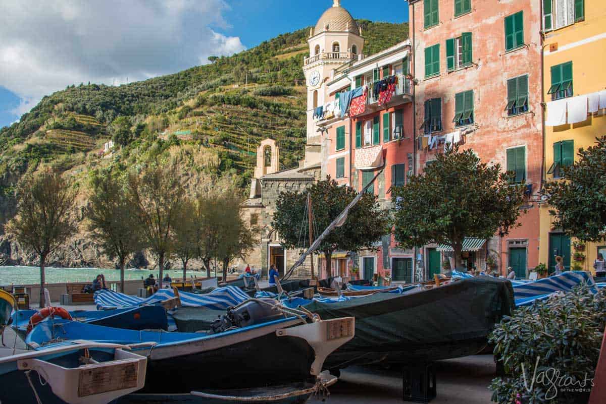 Black fishing boats with b lue covers pulled up onto the street harbour in front of pastel coloured houses on the bay of Cinque Terre. 