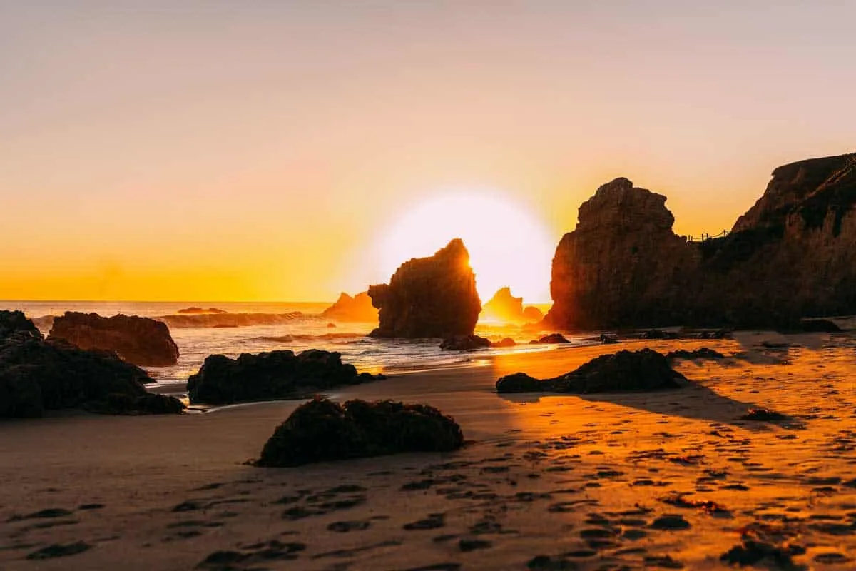 The perfect ball of the sun setting behind the rocks on a Malibu beach.