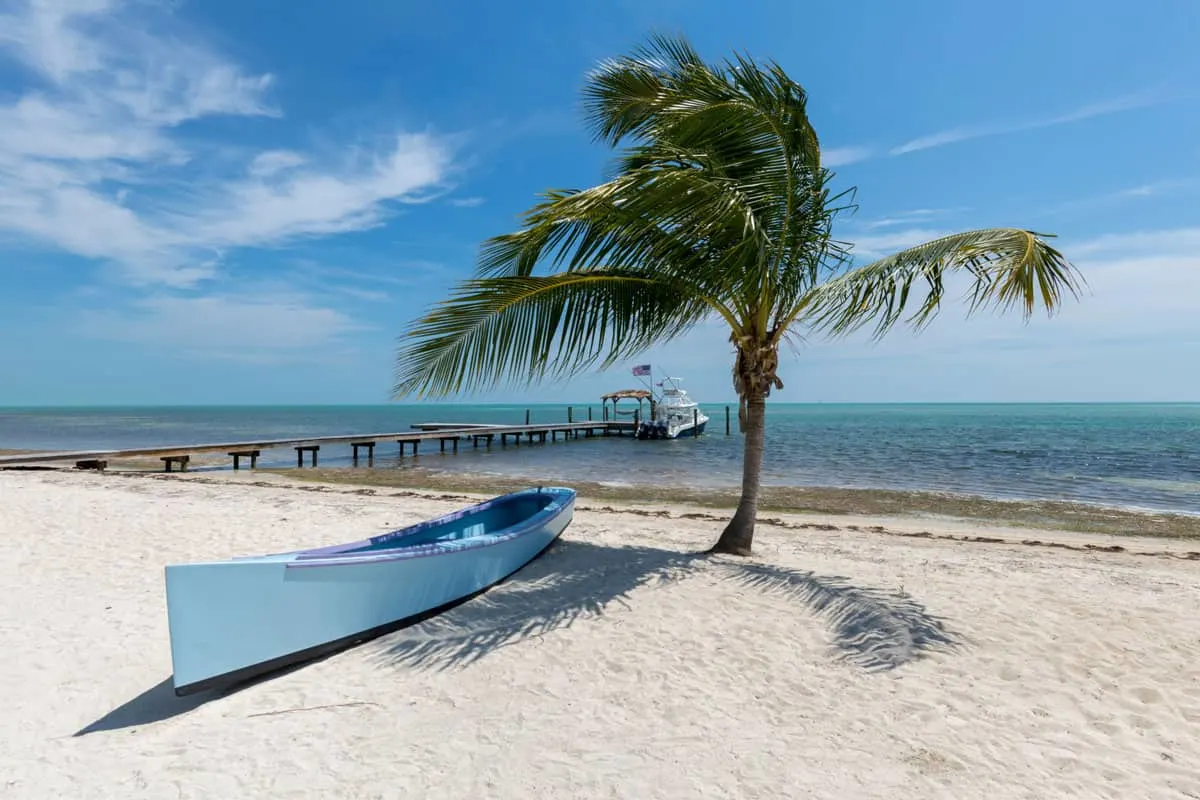 A blue canoe sits under a palm tree on a white beach in Florida Keys