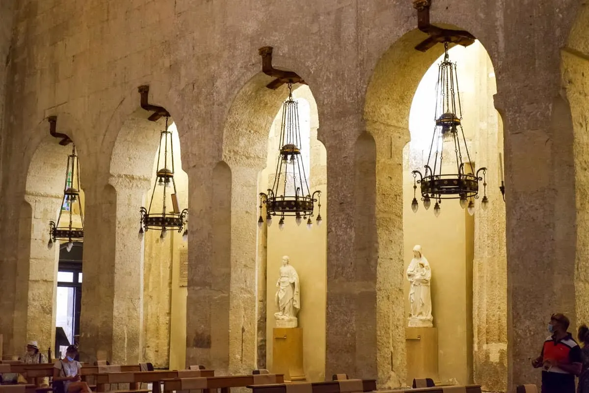 Chandeliers and statues inside a grand stone Italian church.
