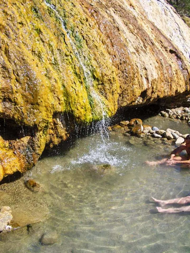 People sitting in hot spring pool beneath a small waterfall at Buckeye springs. 