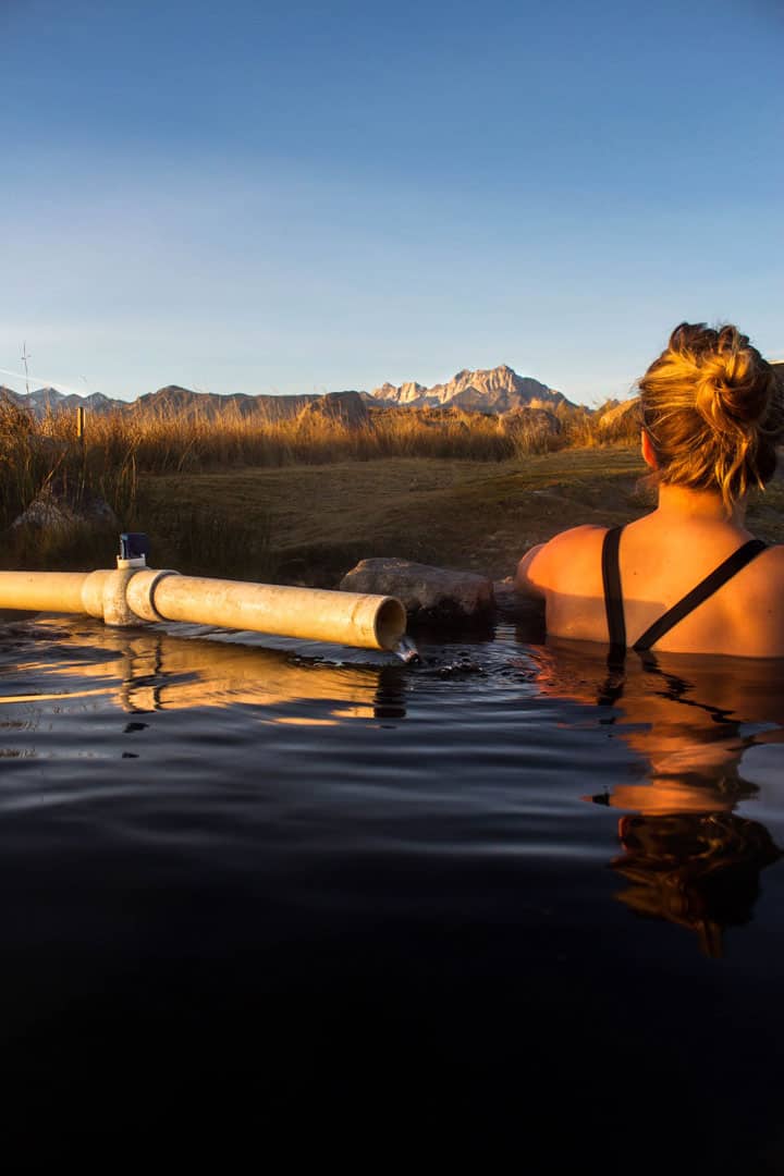 Girl sitting in a natural hot spring pool with views of the eastern Sierra mountains. 